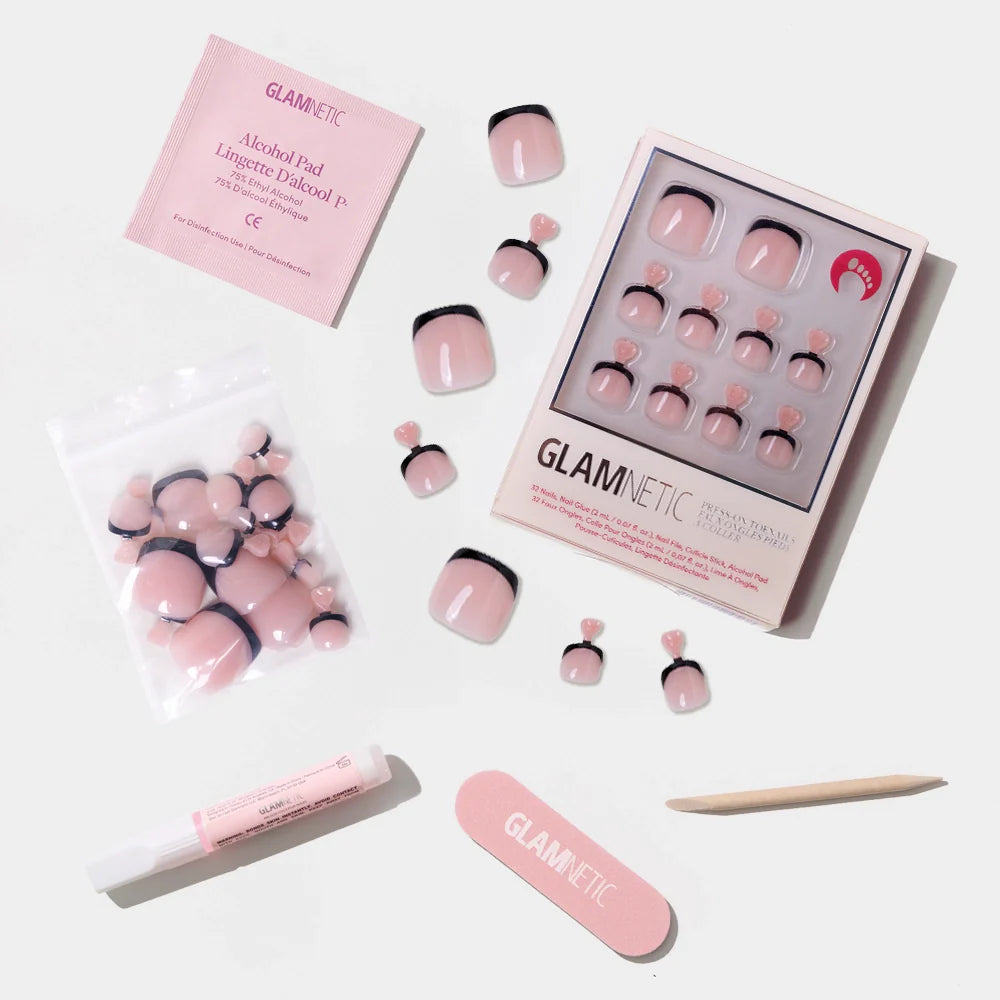 A flat-lay of the Glamnetic nude pink press-on toenail kit with bold black French tips, including glue, file, stick, and alcohol pad.