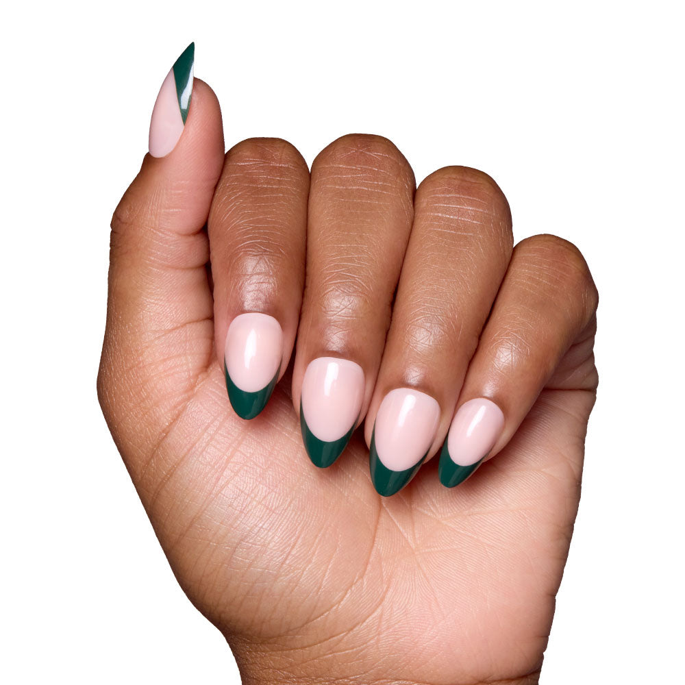 A hand with short almond nails featuring a nude base and dark green French tips, held against a white background, showcases the elegant Château set by glamnetic.