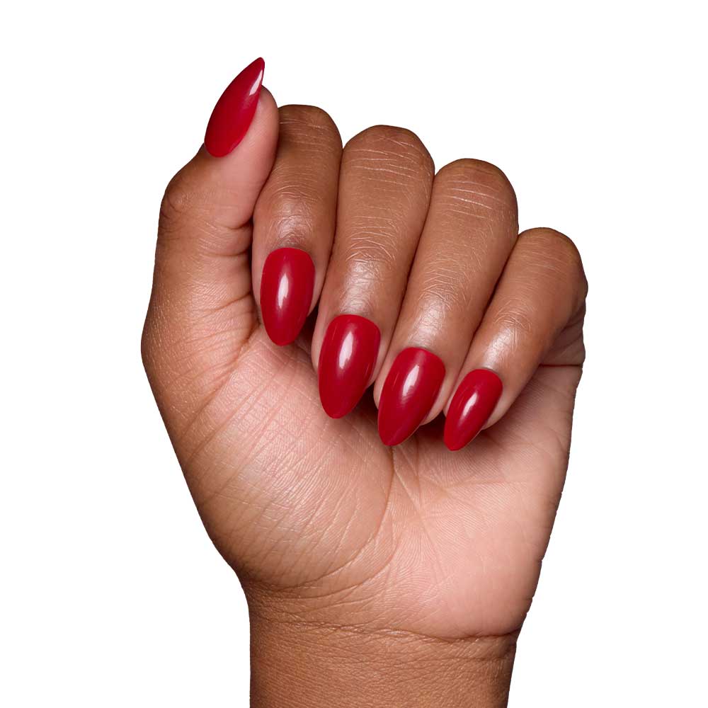 A hand with medium brown skin tone displays the glamnetic Classic Red glossy almond-shaped nails, fingers slightly curled, set against a white background.