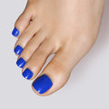 A close-up of a foot showcasing Glamnetic press-on toenails in a vibrant cobalt blue shade with a smooth, high-gloss finish.