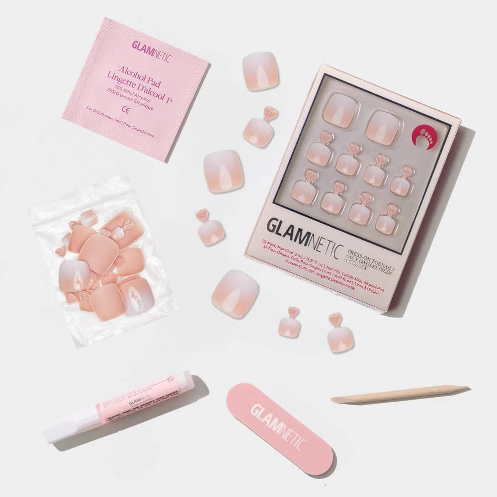 A flat-lay of the Glamnetic nude ombré press-on toenail kit with a white fade and full nail care accessories.
