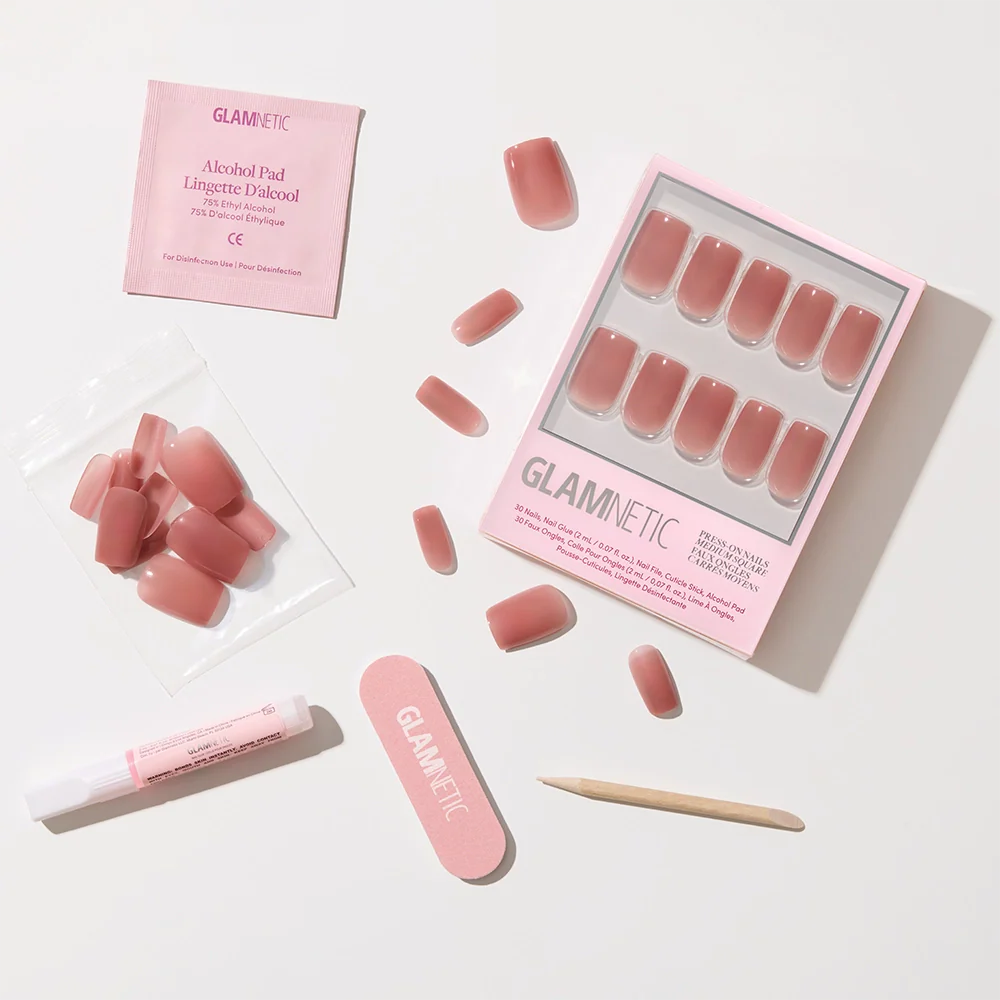 The glamnetic Dusty Pink press-on nails feature a medium square shape and glossy finish, with application tools—nail file, cuticle stick, glue tube, alcohol pad, and extra nails—arranged neatly on a white surface.