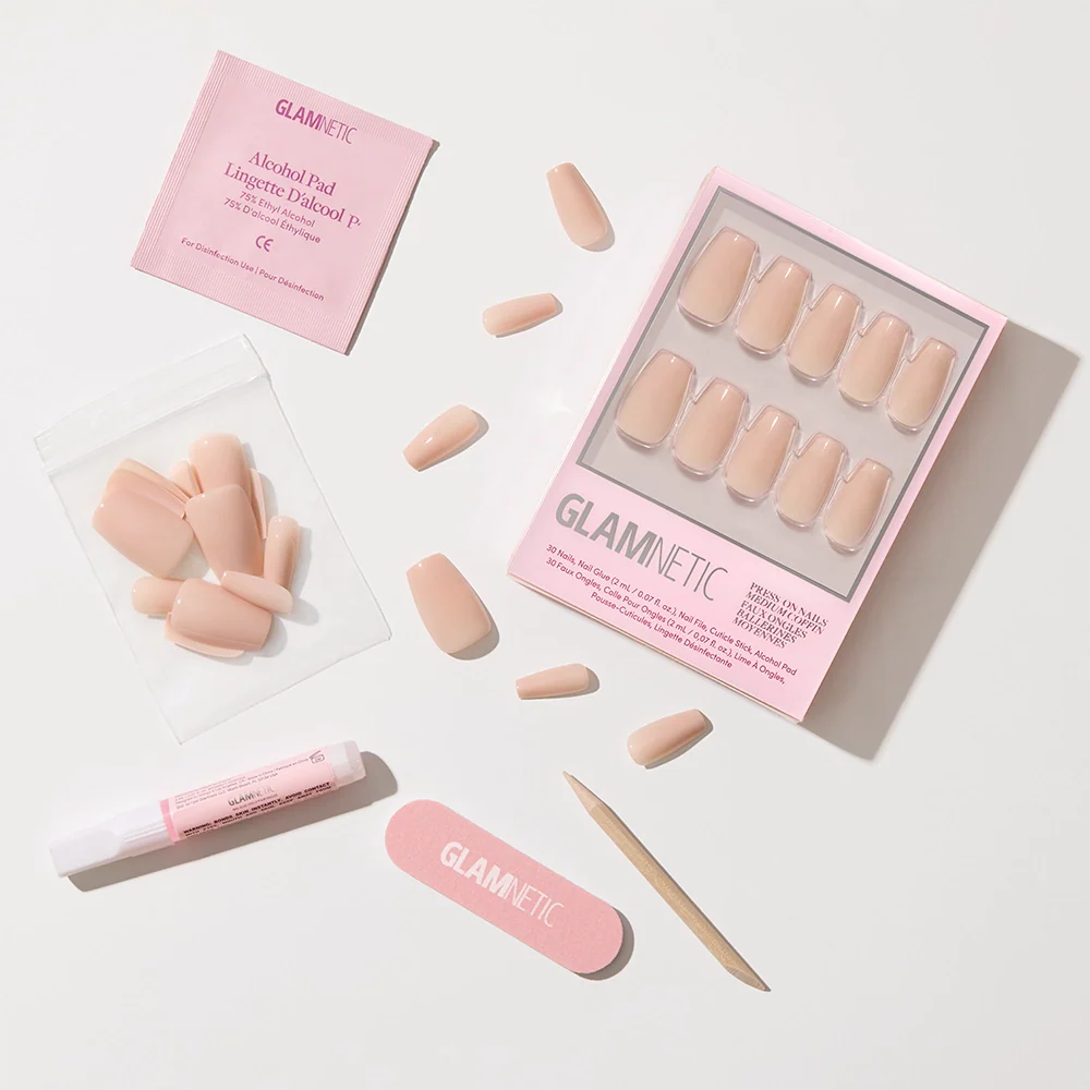 Exposed by glamnetic: a pinky nude, coffin-shaped press-on nail set with a high-shine finish, packed in a pink Glamnetic box with glue, alcohol pad, nail file, cuticle stick, and extra nails, all arranged on a white background.