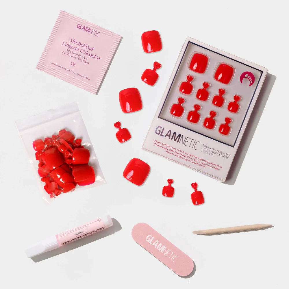 A flat-lay of the Glamnetic bold red press-on toenail kit with full contents laid out, including glue and nail care tools.