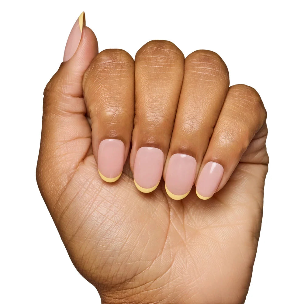 A hand with medium-brown skin displays the glamnetic French Butter Press-On Nail Set—nude base with pastel yellow French tips—against a white background, highlighting its salon-quality durability and stylish look.