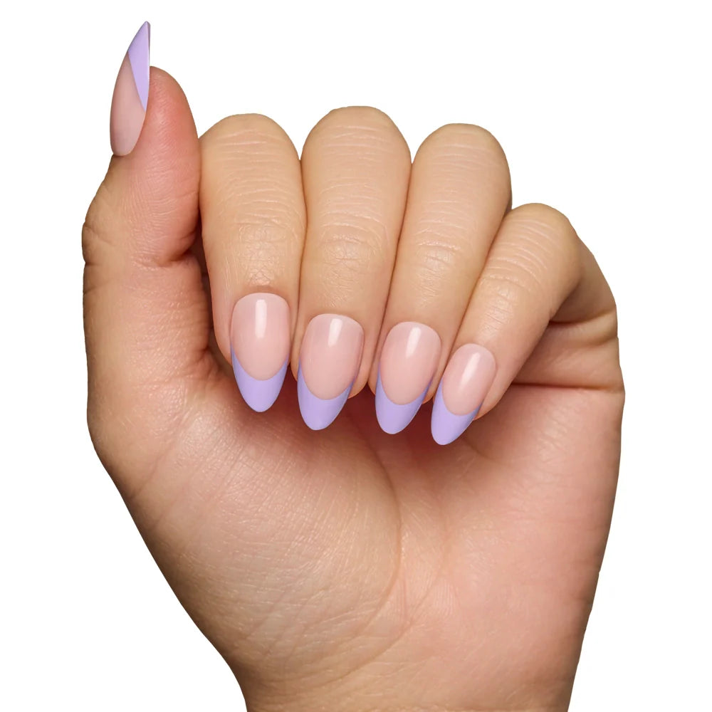 A hand with a manicure featuring glamnetic French Lilac Press-On Nails in a short almond shape, with a nude base and pastel purple tips, displayed against a white background.