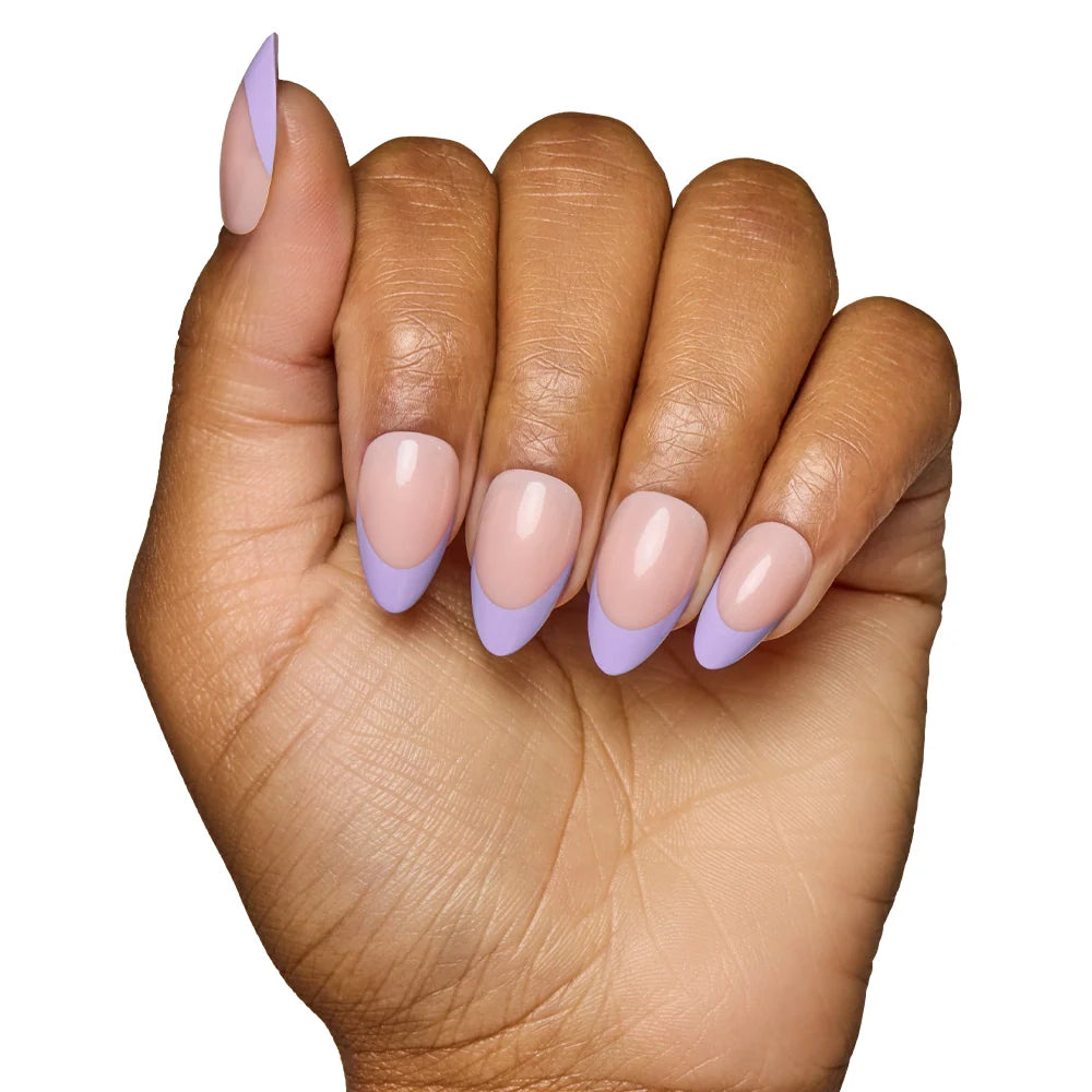 A hand with medium brown skin shows short, almond-shaped nails wearing glamnetic’s French Lilac: a nude base with pastel purple tips, posed against a white background.