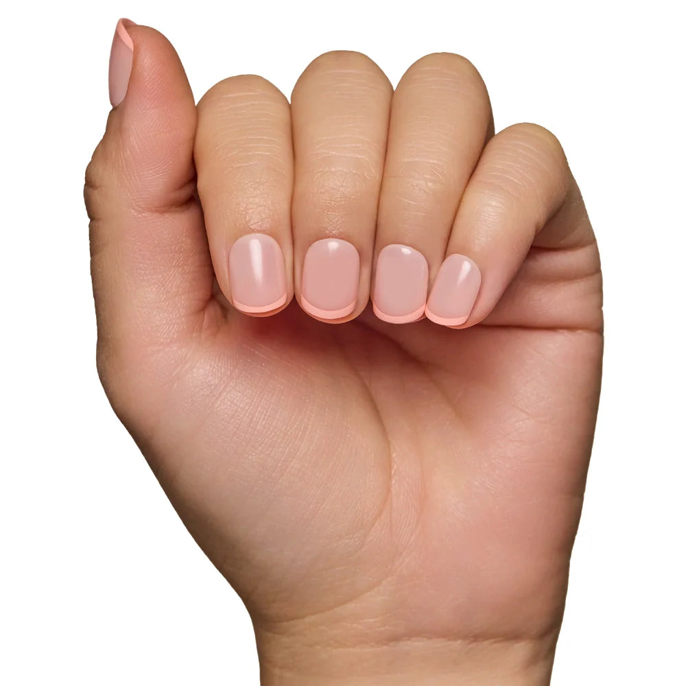 A hand with neatly manicured, light pink French Peach nails by glamnetic, which are vegan and cruelty-free, is shown against a white background. The slightly bent fingers highlight the elegant appearance.