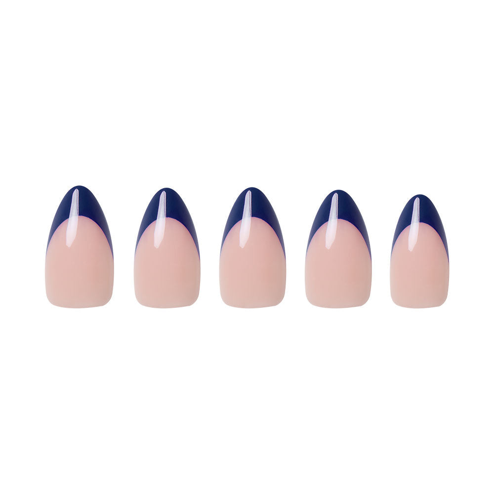 Five short almond nails from glamnetic’s French Riviera set showcase a nude base with navy French tips, each accented by a thin vertical white stripe on the tip, all arranged neatly on a white background for an effortlessly chic look.