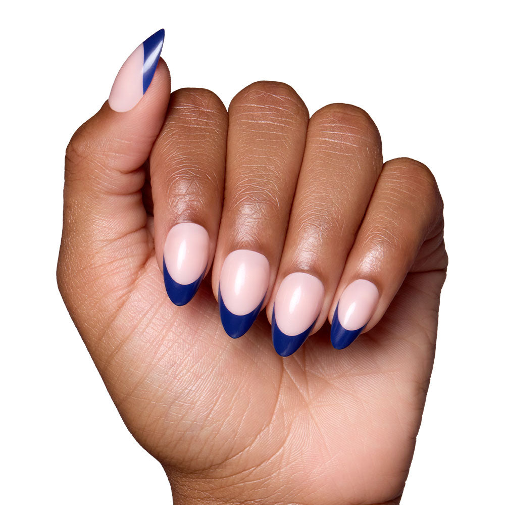 A hand with short almond nails in glamnetics French Riviera—glossy nude base and navy French tips—posed against a white background.