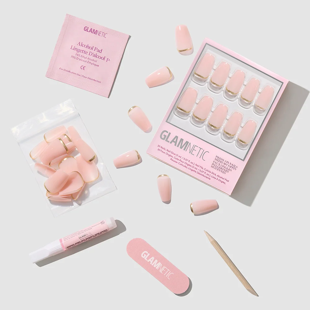 The glamnetic Gold Goals set features pink coffin-shaped press-on nails with gold tips, a nail file, cuticle stick, nail glue, alcohol pad, and extra nails—all arranged on a light gray background for salon-quality manis at home.