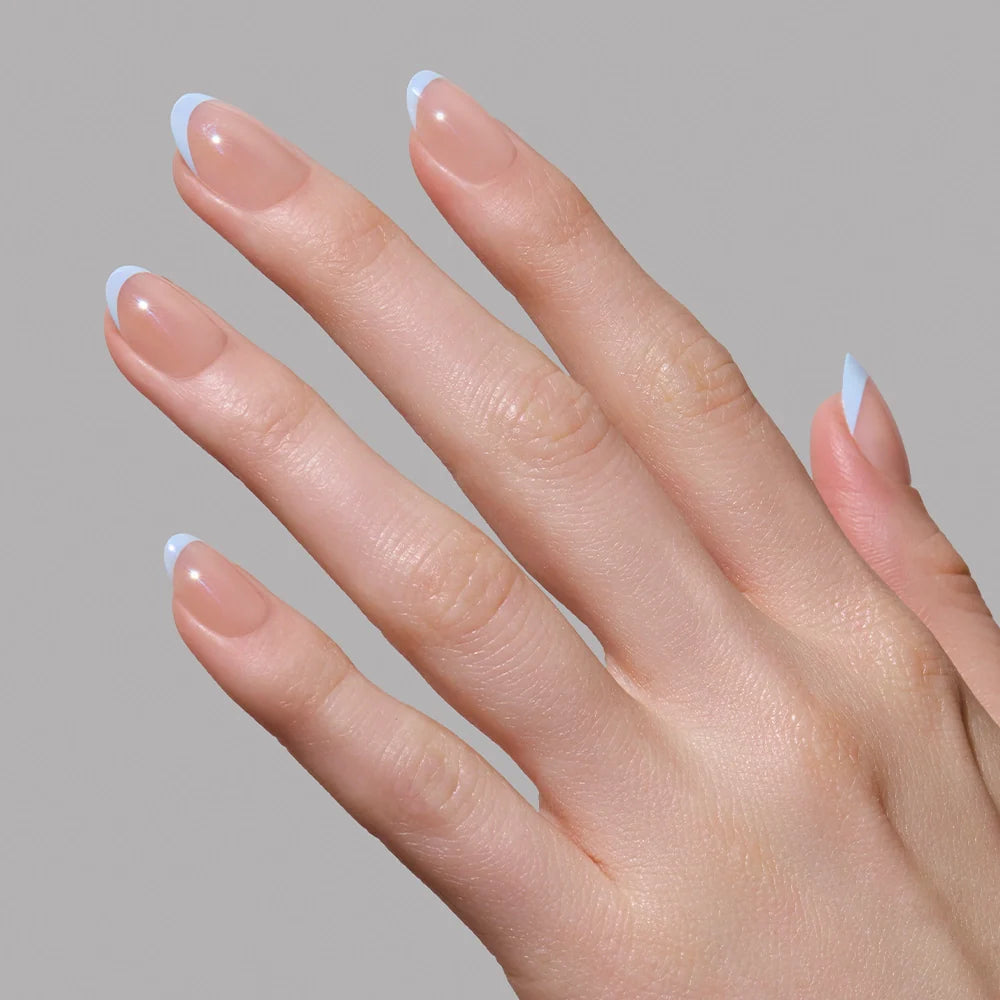 A hand with light skin and neatly manicured nails features glamnetics Into Blue salon-quality periwinkle micro French tips, shown against a plain gray background.