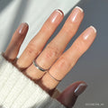 A hand with neat French tips on short squoval nails, adorned with three thin silver rings and a cozy white knit sweater—perfectly showcasing the elegant La Perle set by glamnetic.