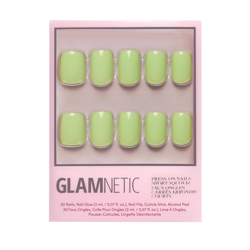 A box of glamnetic Light Sage press-on nails in a short squoval shape with a pastel green glossy finish. Packaging shows ten nails in two rows and includes product details in English and French.