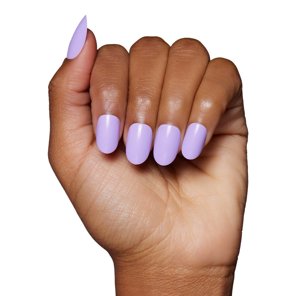 A hand with medium brown skin displays neatly manicured glamnetic Lilac press-on nails, featuring glossy pastel lavender polish, against a white background.