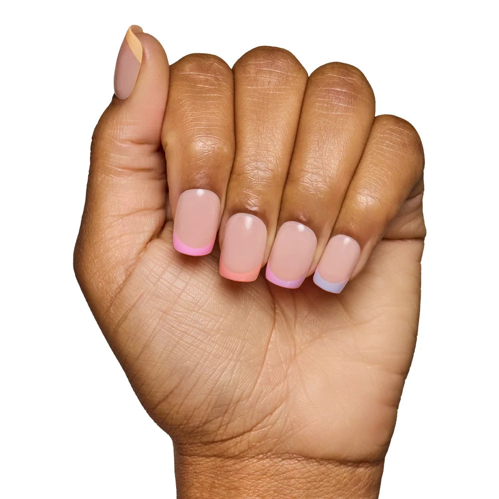 A hand with medium brown skin shows off French tips in pastel pink, blue, and yellow over a nude base. This trendy look uses Macarons Press-On Nails by glamnetic and is set against a white background.