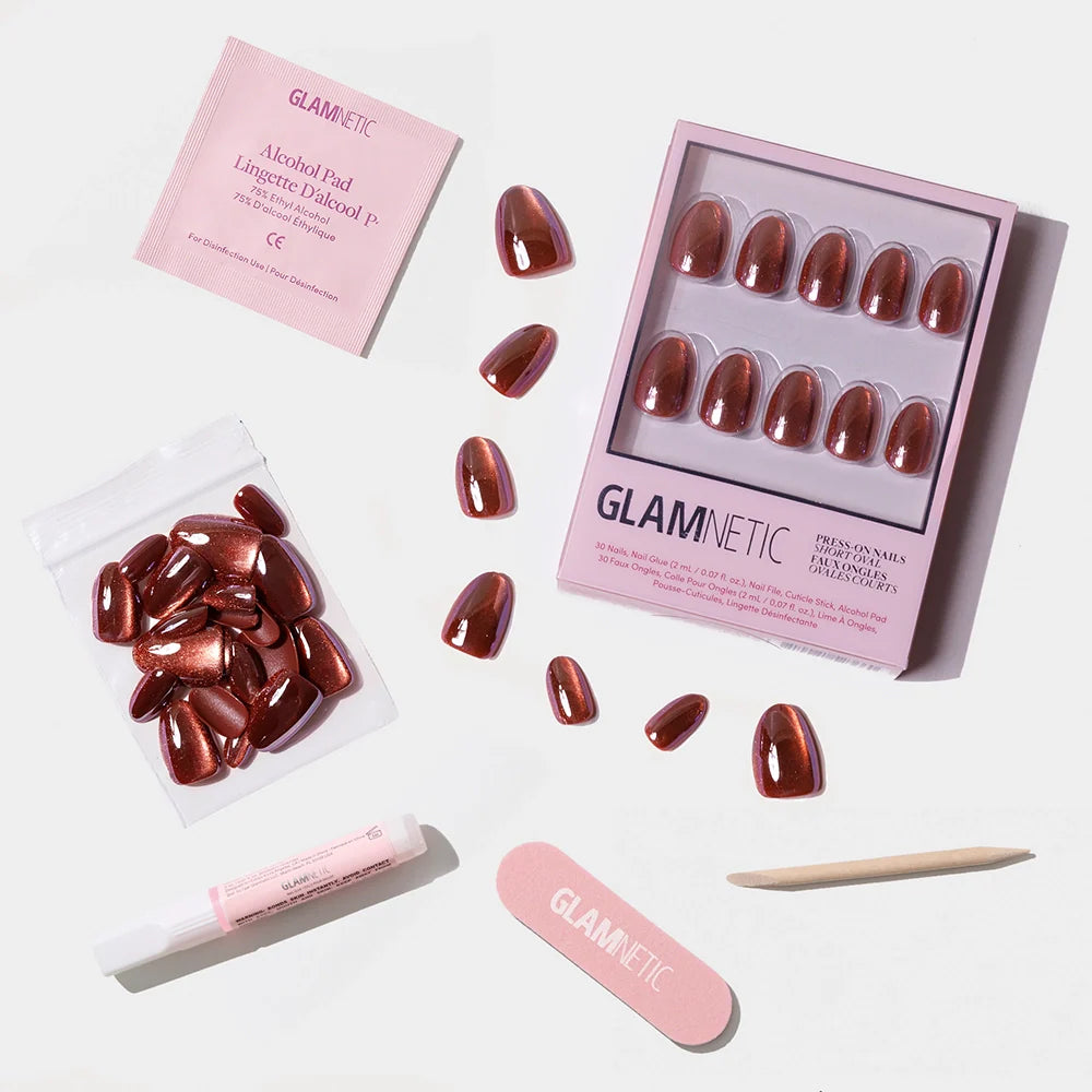 The Magnetic Moscow press-on nails by glamnetic, in metallic reddish-brown short ovals, are shown on a white background with extra nails, cuticle stick, nail glue, nail file, and an alcohol pad.