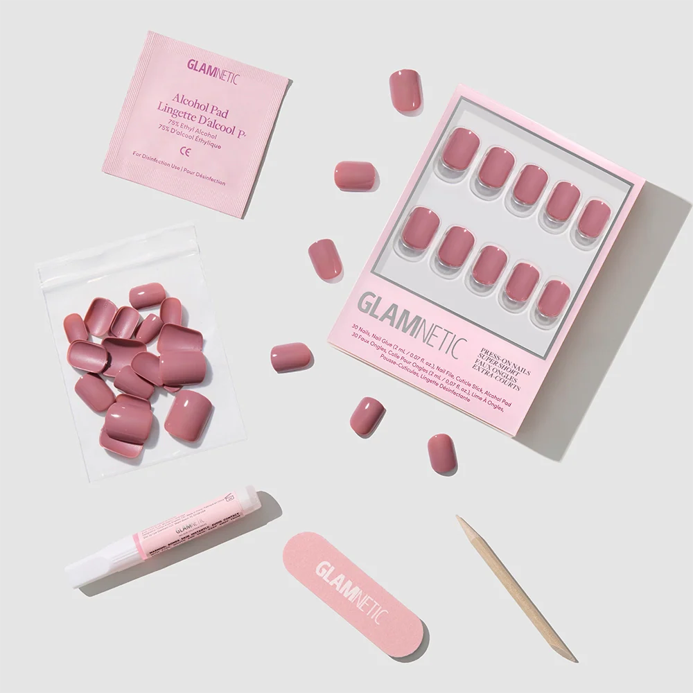 A flat lay of the glamnetic Mauve Cutie press-on nails kit featuring glossy mauve round nails, extra nails, an alcohol pad, nail file, cuticle stick, nail glue, and a small resealable pouch on a light grey background.