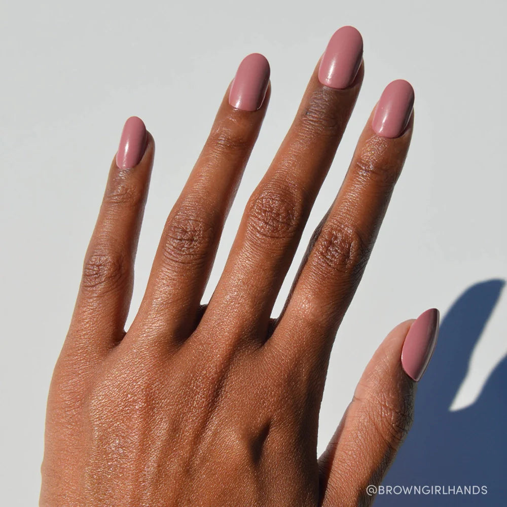 A hand with medium brown skin and neatly manicured nails painted in Mauve Mood by glamnetic is shown against a plain white background, with the @BROWNGIRLHANDS logo in the bottom right corner.