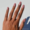 A hand with medium brown skin and neatly manicured nails painted in Mauve Mood by glamnetic is shown against a plain white background, with the @BROWNGIRLHANDS logo in the bottom right corner.