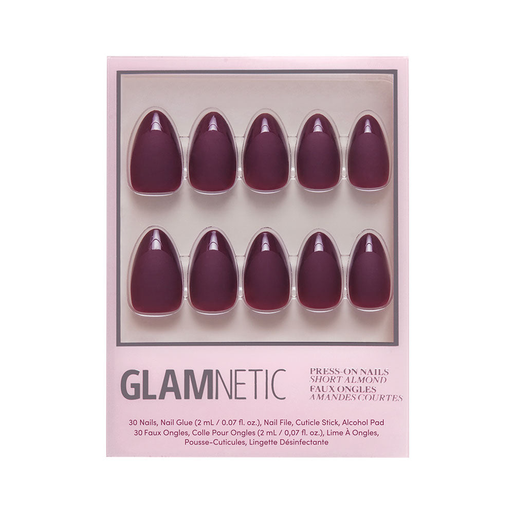 A box of glamnetic Merlot press-on nails in short almond shape with a deep purple matte finish, arranged in two rows of five, featuring product details and glamnetic branding on the packaging.