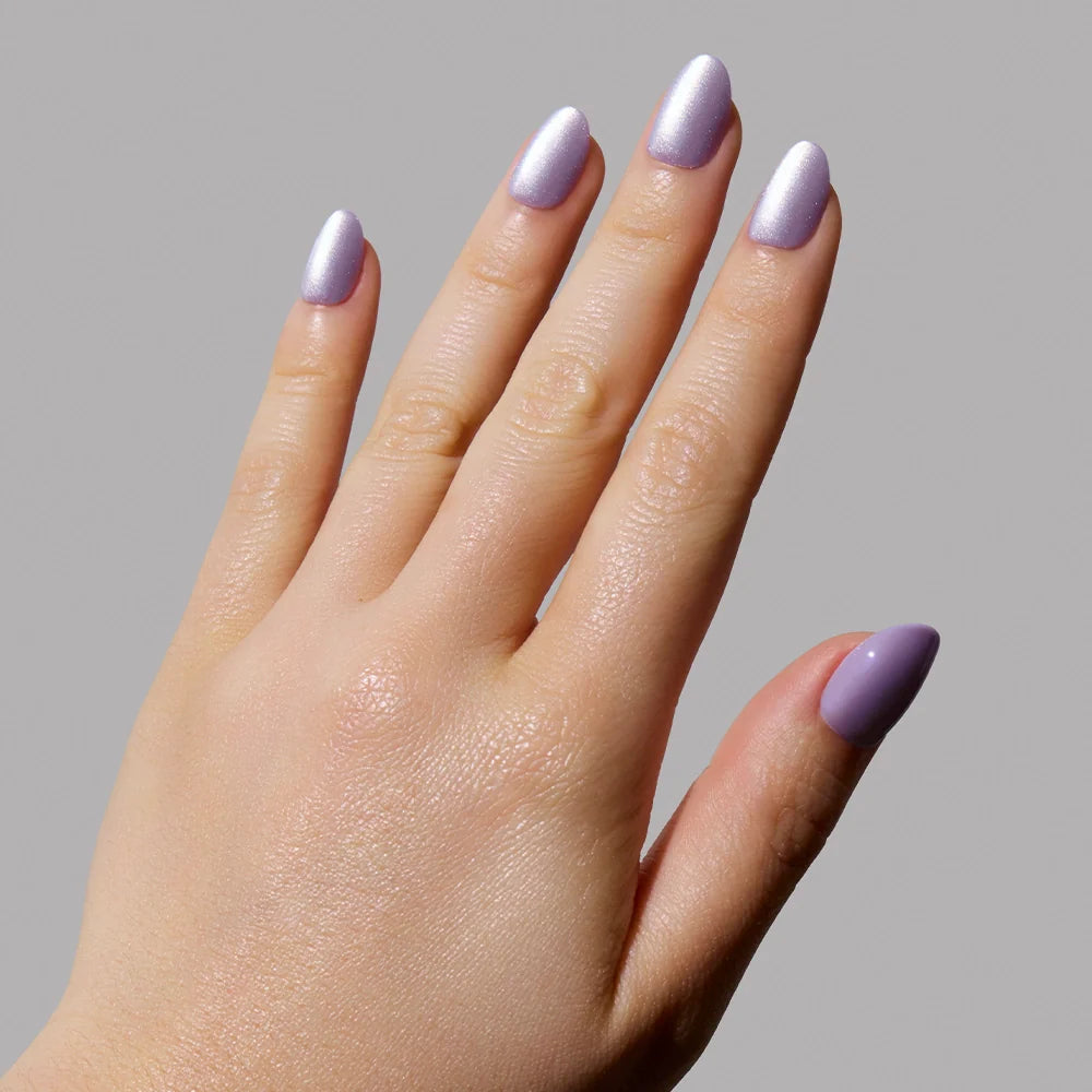 A hand with manicured nails painted in glamnetic’s Mermaids Tail iridescent purple is shown against a plain gray background.