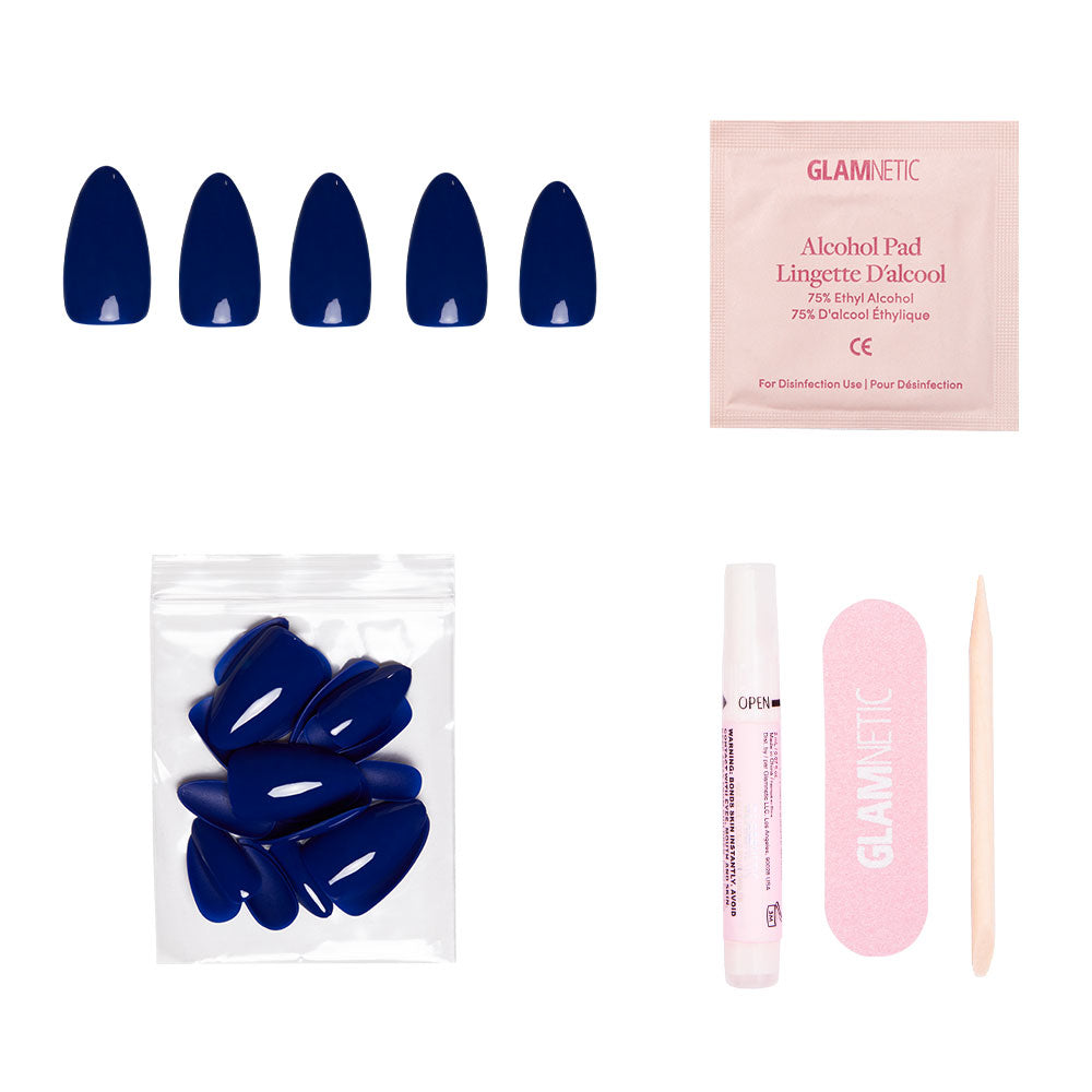 The glamnetic Midnight Blue set includes vegan, cruelty-free navy press-on nails, an alcohol pad, extra nails, nail glue, a pink nail file, and a wooden cuticle stick—all beautifully arranged on a white background.