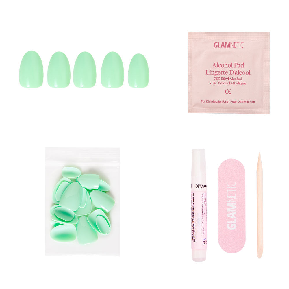 The glamnetic Mint Green press-on nail set includes glossy short oval nails, an alcohol pad, extra nails, an adhesive tube, a pink nail file, and a wooden cuticle stick, all displayed on a white background.