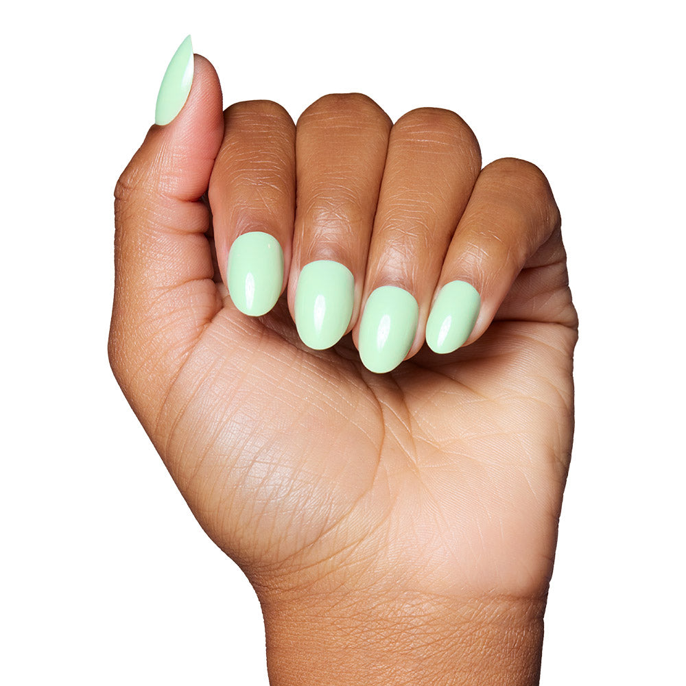 A hand with medium brown skin shows short, oval nails painted in glamnetic’s Mint Green—a glossy, pastel mint shade—against a white background.