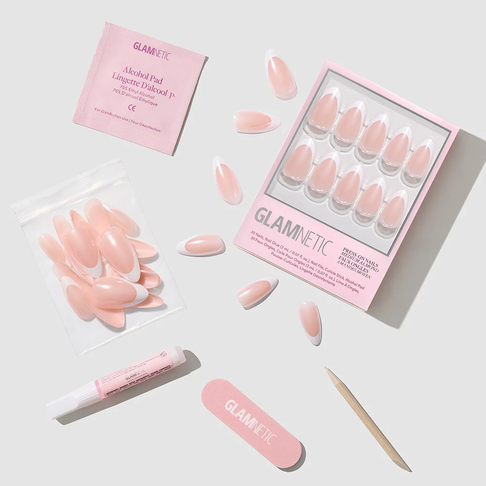 A flat lay of the glamnetic Mother Pearl Press-On Nails kit displays glossy pink nails, a wooden cuticle stick, nail file, alcohol pad, and glue arranged on a light gray background.