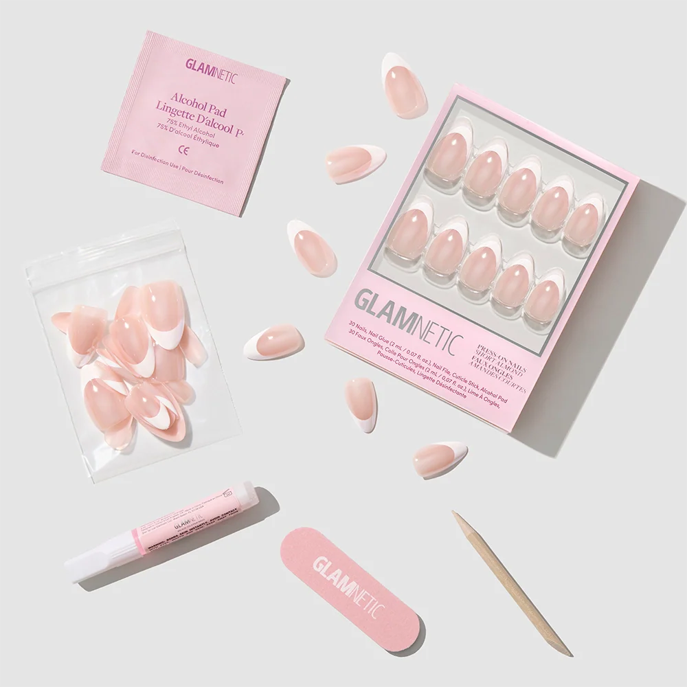 A set of Glamnetic "Mrs." pink and white French tip nails in a short almond shape come with nail glue, alcohol pad, nail file, cuticle stick, and extra nails, all neatly arranged on a light background. Packaging displays the Glamnetic logo.