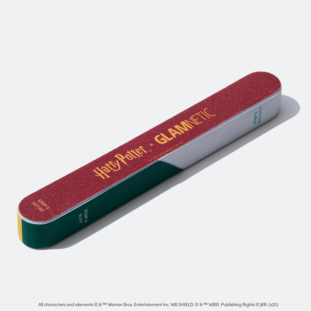 The glamnetic Harry Potter™ x Glamnetic 7-in-1 Nail Buffer features a maroon surface with a yellow logo, plus green and white sides with text—perfect for salon-quality nails. Shown resting on a plain, light background.