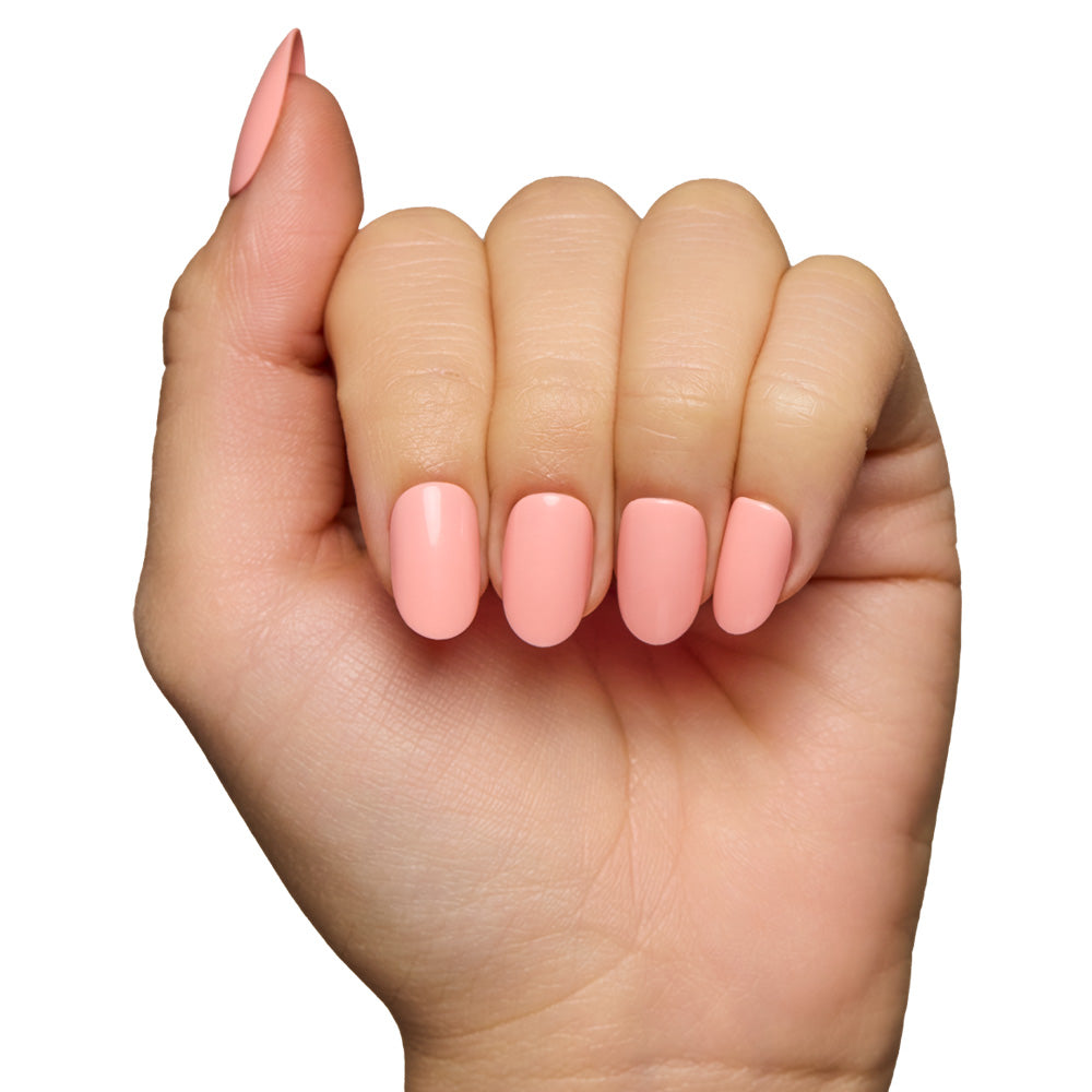 A hand with fingers slightly curled showcases glamnetic’s reusable Peach Coral nails, painted in a glossy pastel peach shade, against a white background.