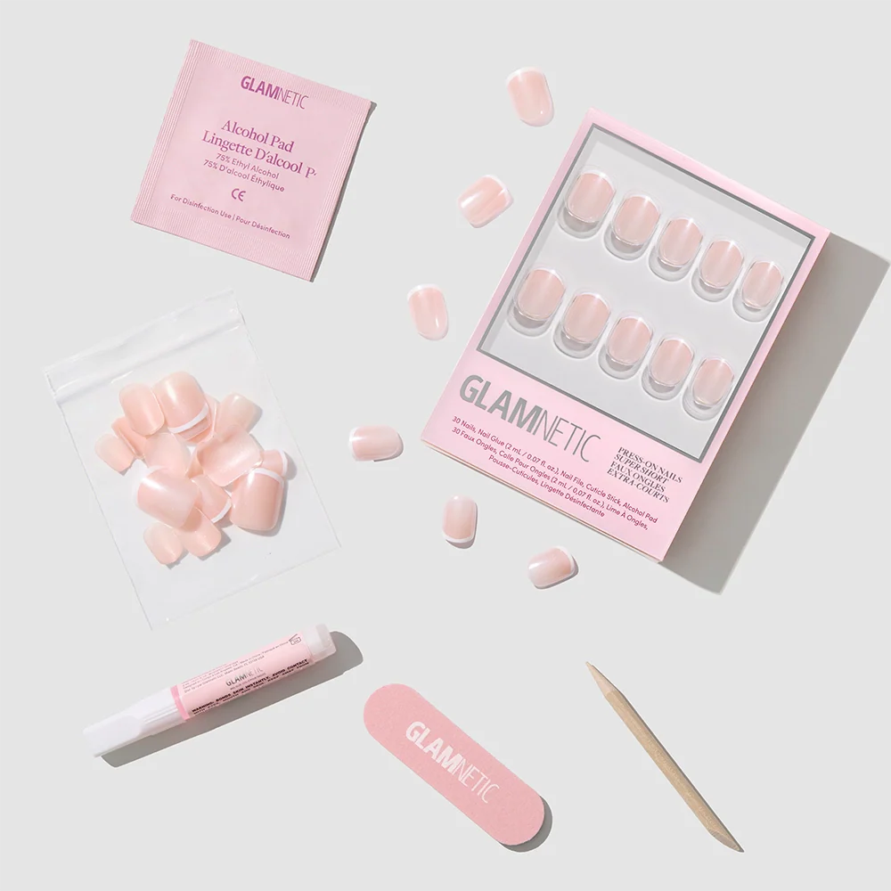 The Pearly Please Press-On Nails by glamnetic, featuring a glossy glazed finish, come with a pink nail file, wooden cuticle stick, alcohol pad, nail glue, and extra nails, all neatly arranged on a light gray background.