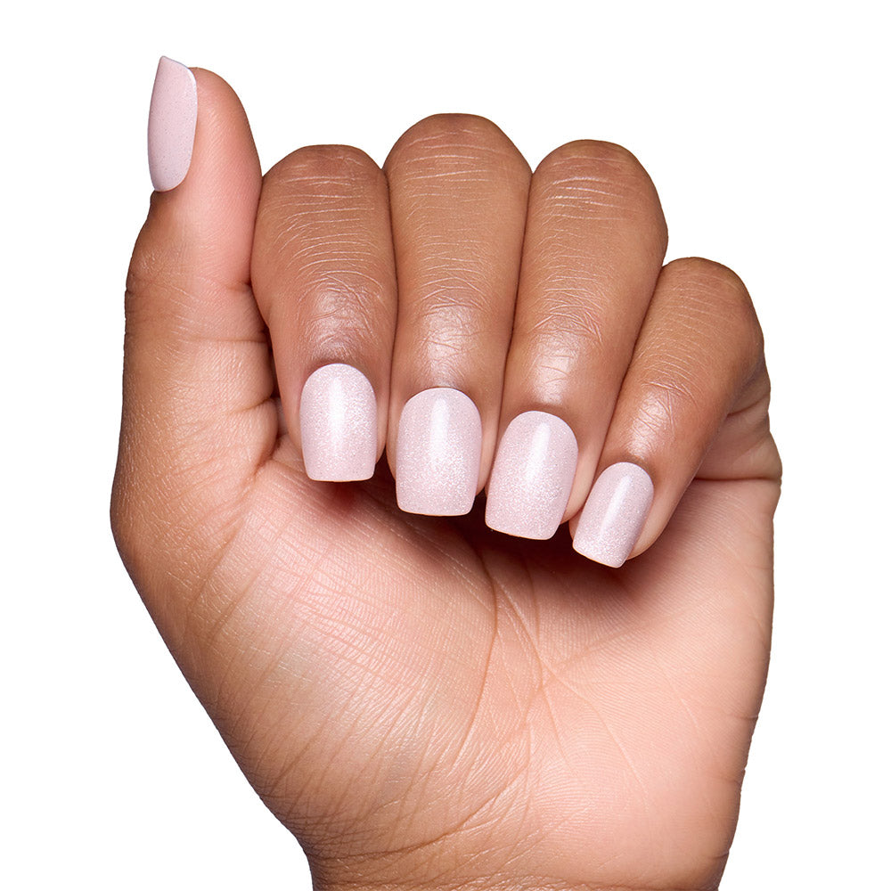A hand with medium-brown skin displays short, squoval nails painted in glamnetic’s Pinky Promise—a light, shimmery blush pink—against a white background.