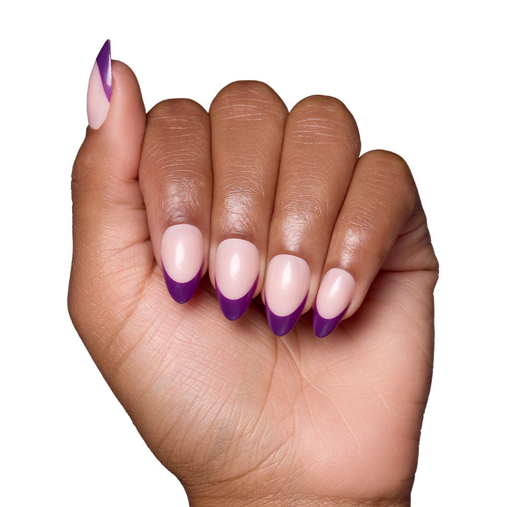 A hand with short almond nails from glamnetics Plum set showcases a nude base with dark purple French tips, all against a white background.