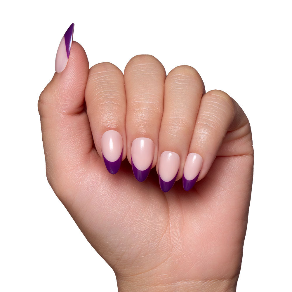 A hand with short almond nails featuring glamnetic’s Plum press-ons: a light pink base with bold, dark purple French tips, against a white background.