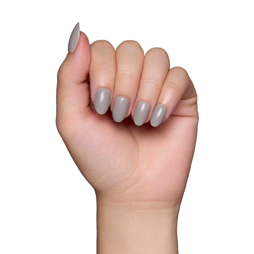 A light-skinned hand with slightly curled fingers displays glamnetics Pure Gray nails, featuring a smooth, glossy light grey finish, set against a plain white background.