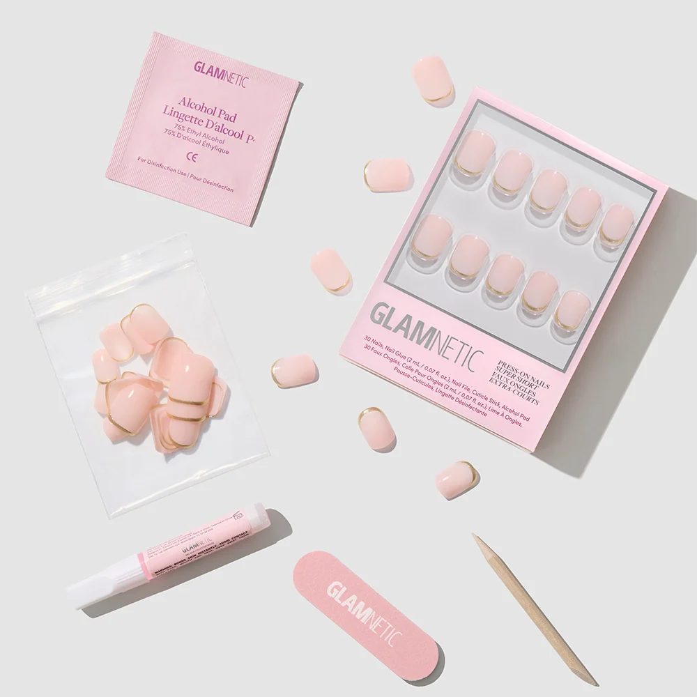 The "Quiet Luxury" press-on nails by glamnetic come in a set with glue, nail file, wooden cuticle stick, alcohol pad, and extra nude nails featuring gold French tips—all arranged neatly on a light gray background.