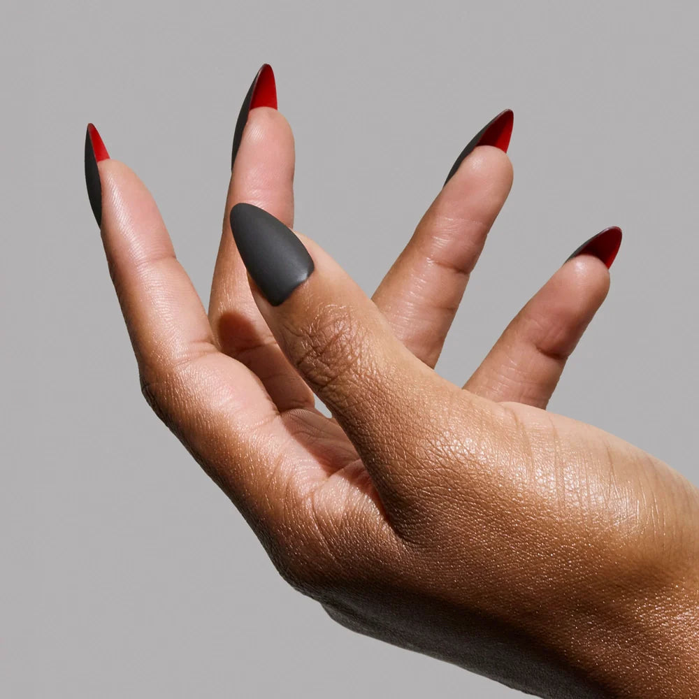 A hand with long, black matte almond nails from glamnetics Red Bottom set, featuring a bold red underside, posed against a gray background for a luxurious press-on nails look.