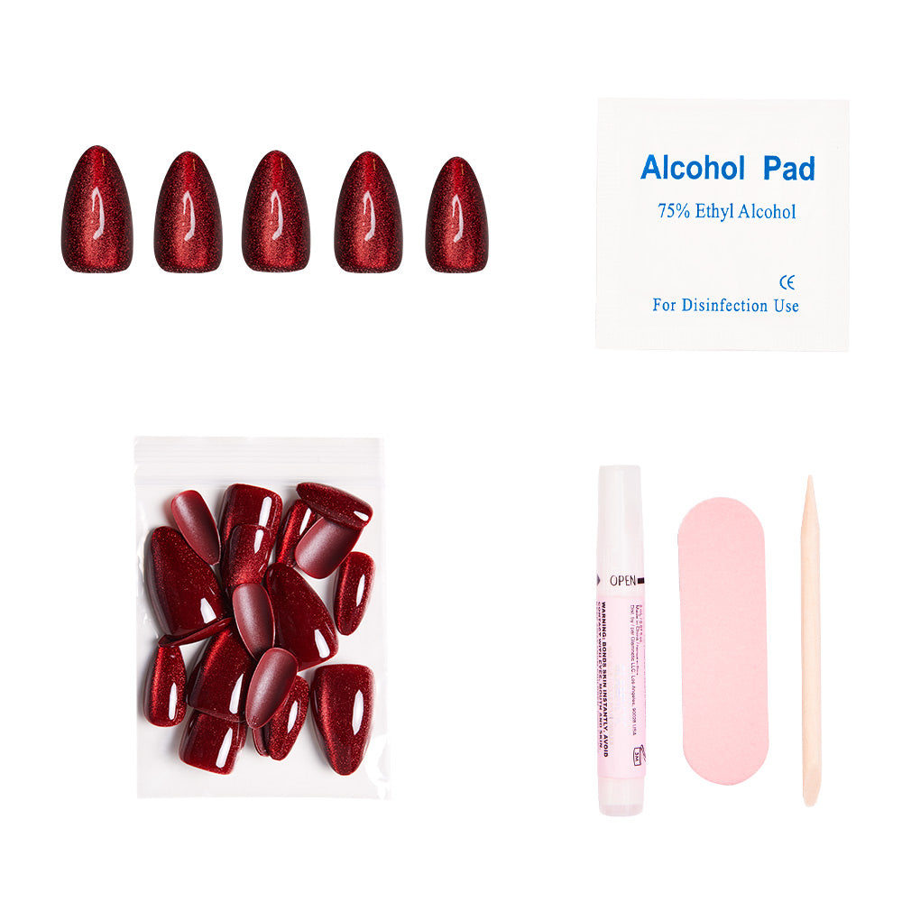 The glamnetic Ruby Slipper set includes short almond red glitter press-on nails, an alcohol pad, extra nails, nail glue, a pink file, and a wooden cuticle stick—all arranged on a white background.
