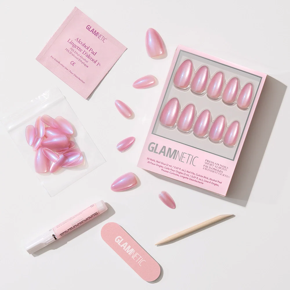 The glamnetic Seaspell set includes pink iridescent, short almond press-on nails with a velvet shimmer, plus nail glue, a wooden cuticle stick, file, extra nails, and an alcohol pad—all displayed on a white background.