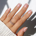 A hand flaunts the glamnetic She’s a Pearl Press-On Nails—a French tip manicure with white tips and a subtle diagonal pinky accent—paired with stacked silver rings and a white ribbed sleeve for an effortlessly chic look.