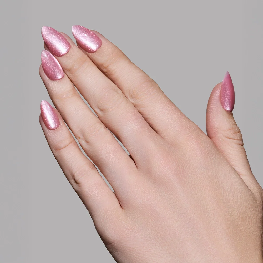 A hand with long, almond-shaped nails painted in glamnetic's Shine for You, a shimmery pink polish, is shown against a plain gray background.