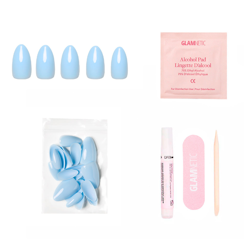 The glamnetic Soft Blue set includes glossy short almond press-on nails, a pink alcohol pad, extra nails in a clear bag, nail glue, a pink nail file, and a wooden cuticle stick—all displayed on a white background.