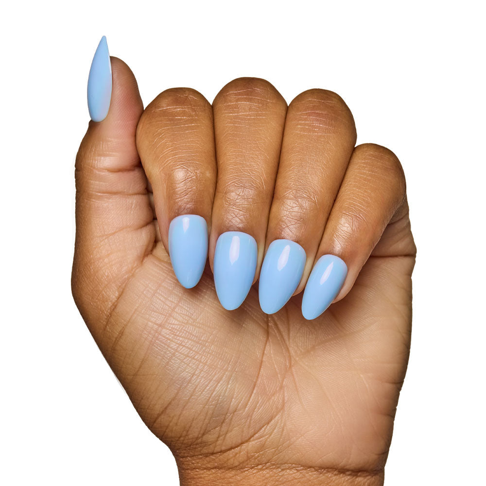 A hand with medium brown skin tone displays short almond nails painted with glamnetics Soft Blue Nail Set, featuring a glossy finish, elegantly set against a white background.