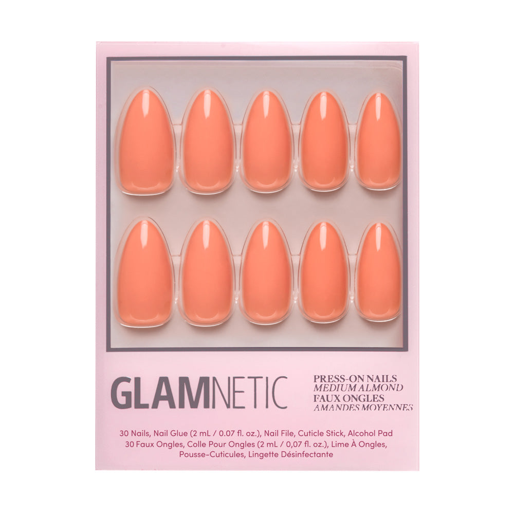A package of glamnetic Soft Tangerine press-on nails, featuring 10 pastel orange acrylics, is displayed in a clear plastic tray on a pink background.