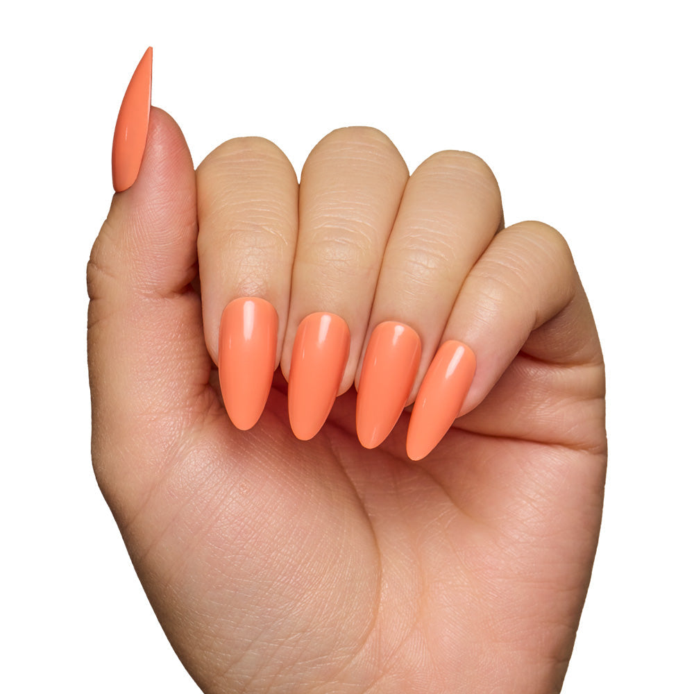 A hand with long almond-shaped nails, coated in glamnetics Soft Tangerine—a glossy pastel orange shade—stands out against a white background, highlighting the fresh elegance of this nail set.