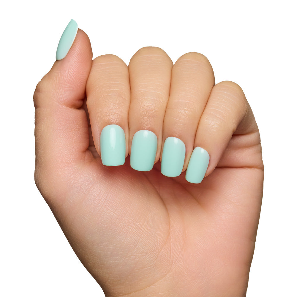 A light-skinned hand with fingers curled inward displays neatly manicured glamnetic Soft Teal Short Squoval Nails in a pastel mint green, set against a white background.