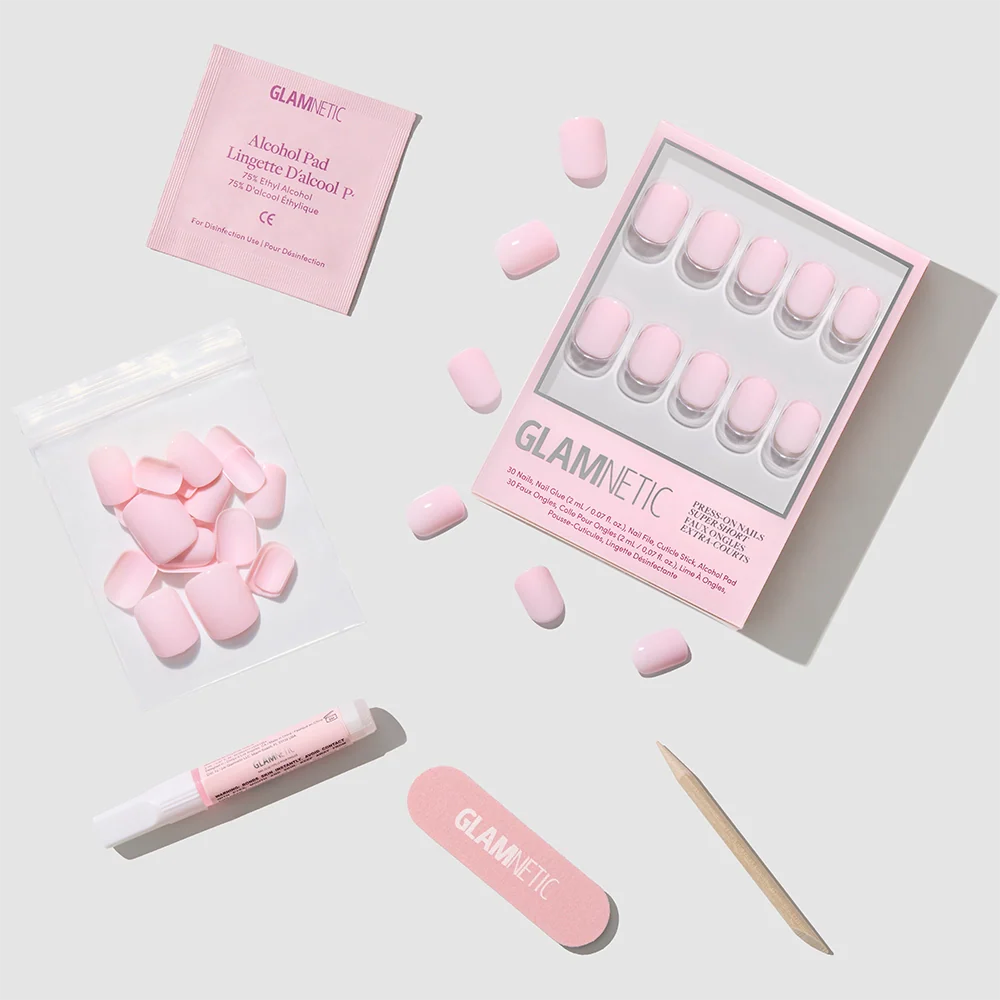 A flat lay of glamnetic’s Sugar BB kit, featuring glossy pink press-on nails, loose super short nails in a bag, an alcohol pad, nail glue, a file, and a cuticle stick—all on a light gray background.